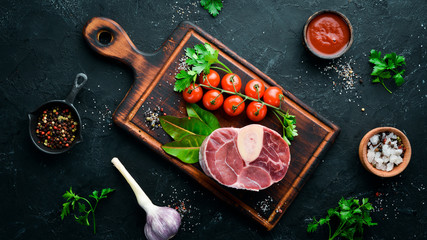 Raw fresh cross cut veal shank for making Osso Buco with spices and herbs on a black background. Top view. Free space for your text.