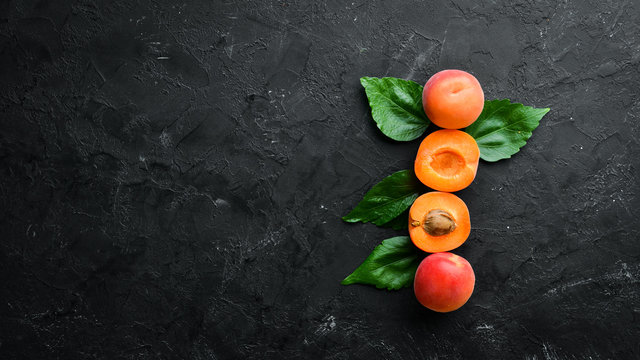 Fresh apricots with green leaves on a black background. Rustic style. Top view. Free space for your text.