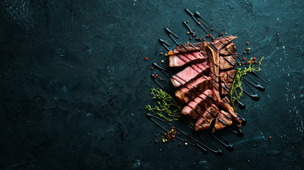 Beef T-Bone steak on a black table. Top view. Free space for text. - obrazy, fototapety, plakaty