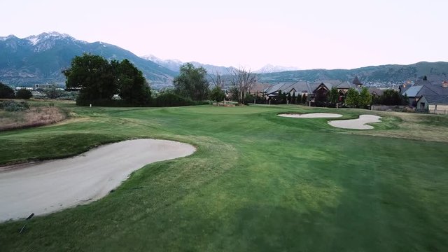 Drone Shot flying over a fairway towards the green on a luxury green golf course. The Wasatch Mountain Range can be seen in the distance.