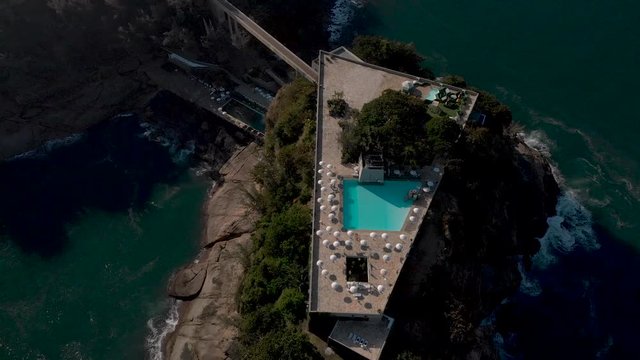 Top down aerial view of a recreational construction on a small island on the coast of Rio de Janeiro seen from above at sunset with umbrellas casting a shade around the pool