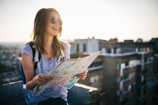 Happy young woman with a city map and a backpack travelling