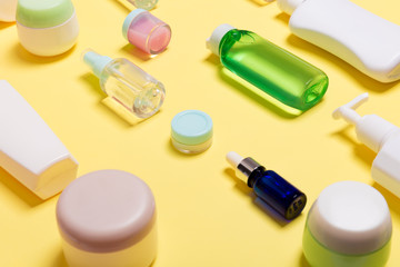 Naklejka premium Composition of different sized cosmetic jars and bottles on yellow background. Beauty care concept with copy space