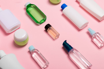 Top view of cosmetic containers, sprays, jars and bottles on pink background. Close-up view with empty space for your design