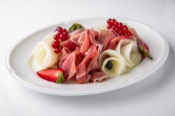Slicing gourmet meat, prosciutto from beef and pork with berries, cheese, vegetables. Banquet festive dishes. Gourmet restaurant menu. White background.