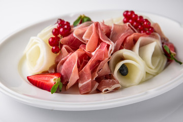 Slicing gourmet meat, prosciutto from beef and pork with berries, cheese, vegetables. Banquet festive dishes. Gourmet restaurant menu. White background.