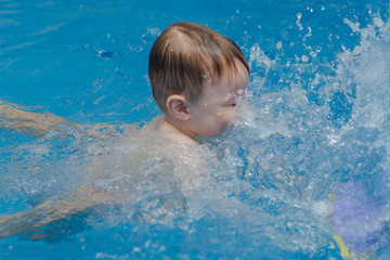 Fototapeta na wymiar little boy swims in the pool and splashes