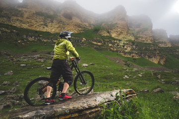 Side view of a man on a mountain bike standing on a rocky terrain and looking at a rock. The concept of a mountain bike and mtb downhill