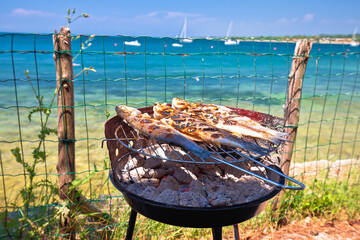 Fish on the grill by the mediterranean beach, idyllic vacation food preparing - obrazy, fototapety, plakaty