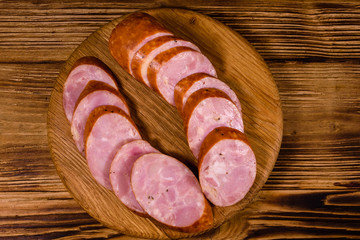 Cutting board with sliced sausage on a wooden table. Top view