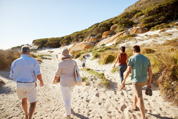 Parents and grandparents walking on beach with young boy running ahead of them