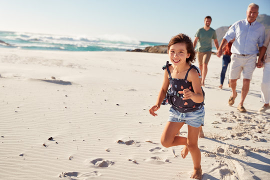 Three generation white family walking together on a sunny beach, young daughter running ahead