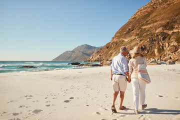Senior white couple walking on a beach together holding hands, full length, back view