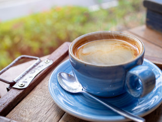 Hot American coffee is in a blue ceramic solution placed on a wooden floor table in cafe with smoke and sunlight.Coffee break in morning/ selective focus