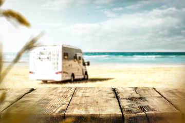 Table background with a wooden board and sunny beach and ocean and a camper van