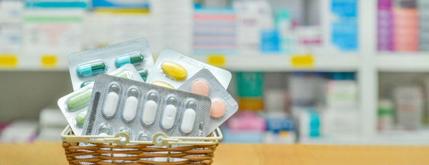 Shopping basket filled with blister packs of medicine on pharmacy drugstore shelves...