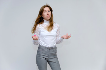 Portrait of a knee-high young pretty brunette girl woman with beautiful long hair on a white background in a white jacket and gray pants. He talks, shows his hands with emotions in various poses.