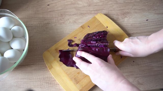 the female hands cut with a knife a red cabbage on a wooden table. Prepare a natural dye for blue Easter eggs