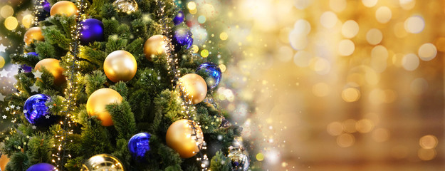 Obraz na płótnie Canvas Christmas tree decorated with Golden and blue balls toys on a blurred, sparkling and fabulous fairy background with beautiful bokeh, copy space, banner format.