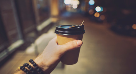 POV, coffee or latte paper cup in a male hand at night