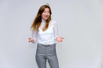 Portrait of a knee-high young pretty brunette girl woman with beautiful long hair on a white background in a white jacket and gray pants. He talks, shows his hands with emotions in various poses.
