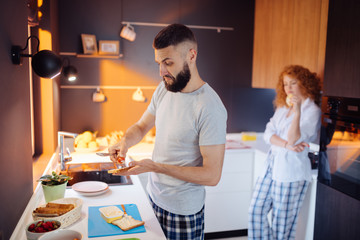 Handsome bearded man putting tomato on the sandwich