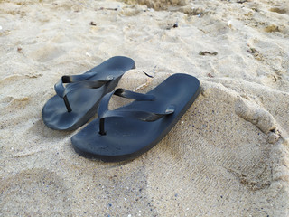 two black slippers on the sand. Flip Flops. Sea. Beach