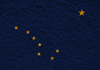 The national flag of the US state Alaska in against a gray wall with stony surface on the day of independence in colors of blue ground and yellow stars. Political and dispute, customs and delivery