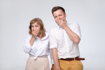 Mature woman and man giggling together covering their mouths with hands trying to be calm