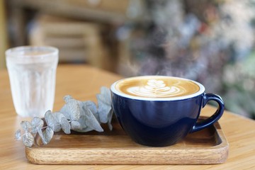 Hot coffee on wooden table, The best cappuccino fresh coffee with smoke. Porcelain coffee cup on table with cold water, Selective focus and free space for text. Industrial food and drink concept.