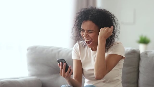 Happy young african american woman winner screaming looking at smartphone