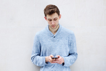 serious young man looking at cellphone by wall