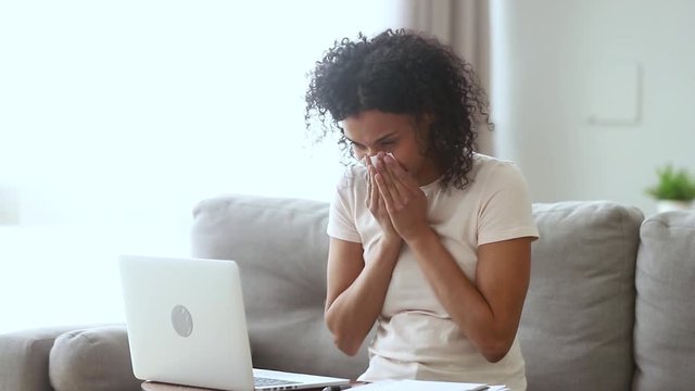 Allergic ill african woman blowing nose sneezing working from home