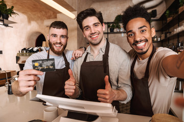 Three cheerful men baristas standing behind the counter