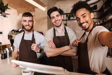 Three cheerful men baristas standing behind the counter