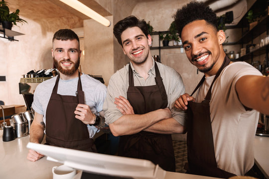 Three cheerful men baristas standing behind the counter