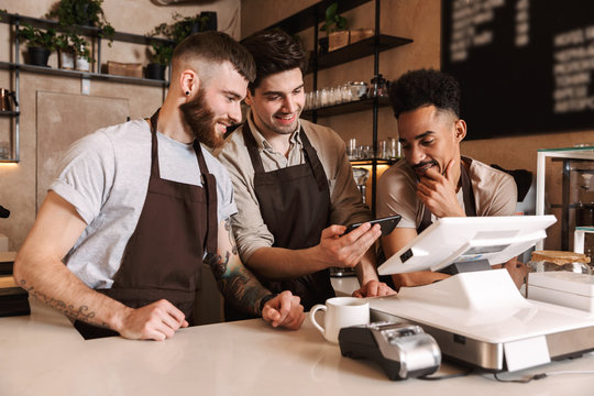 Three cheerful men baristas standing behind the counter