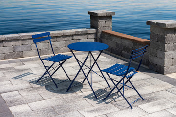 Stone terrace by the sea with bright blue table and two chairs