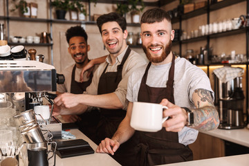 Three cheerful male baristas standing at the coffee shop