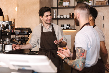 Three cheerful male baristas standing at the coffee shop