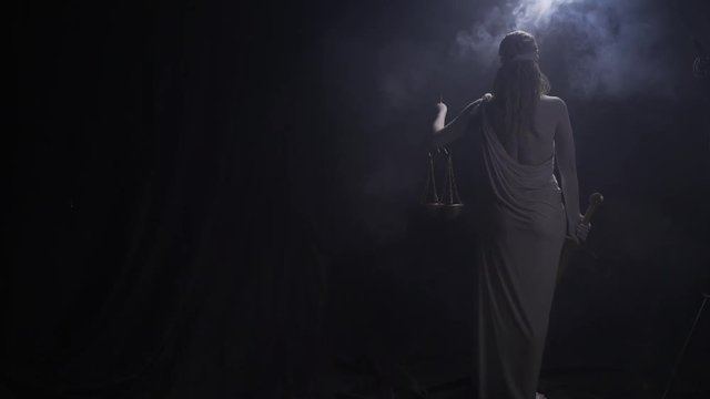 View from the back of Themis, lifting up the scales, with smoke and low lighting
