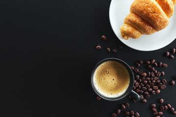hot coffee, bean and butter croissants on black table with soft-focus and over light in the background
