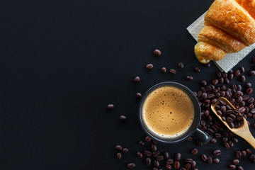 hot coffee, bean and butter croissants on black table with soft-focus and over light in the background