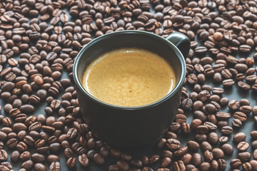 hot espresso and coffee bean on black table with soft-focus and over light in the background. top view and vintage color tone