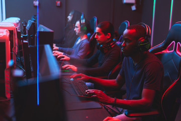 Group of busy multi-ethnic online gamers in casual outfits sitting at table and playing strategy...