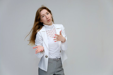 Portrait to the waist of a young pretty brunette girl woman with beautiful long hair on a white background in a white jacket and gray pants. Talks, smiles, shows hands with emotions in various poses.