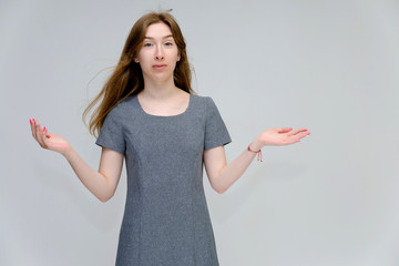 A portrait below belt of a young pretty brunette girl woman with beautiful long hair on a white background in a gray dress. He talks, smiles, shows his hands with emotions in various poses.