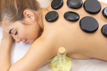 Obraz na płótnie Canvas Spa hot stone massage. Professional beautician massaging female back by stones. Relaxed girl enjoying body treatment at wellness center