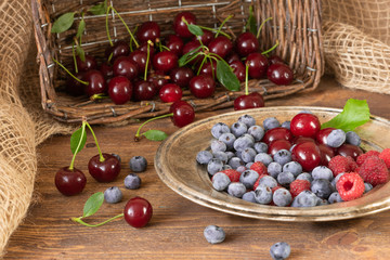 Ripe cherries, raspberries and blueberries on a wooden background