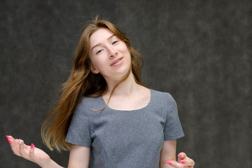 Portrait below the chest of a young pretty brunette girl woman with beautiful long hair on a gray background in a gray dress. He talks, smiles, shows his hands with emotions in various poses.